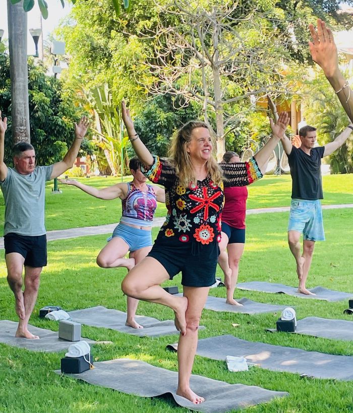 Participants engage in a group yoga session outdoors at Velas Resorts, showcasing balance and relaxation amidst greenery.
