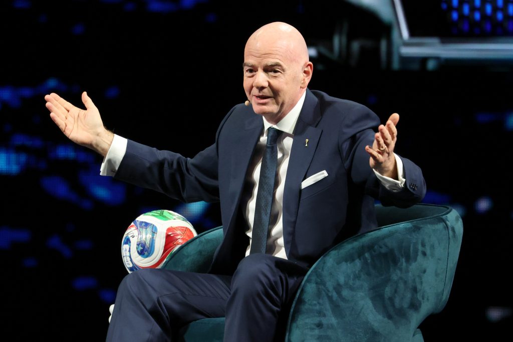 A speaker gestures while seated in a chair at the America Business Forum, with a soccer ball beside them.