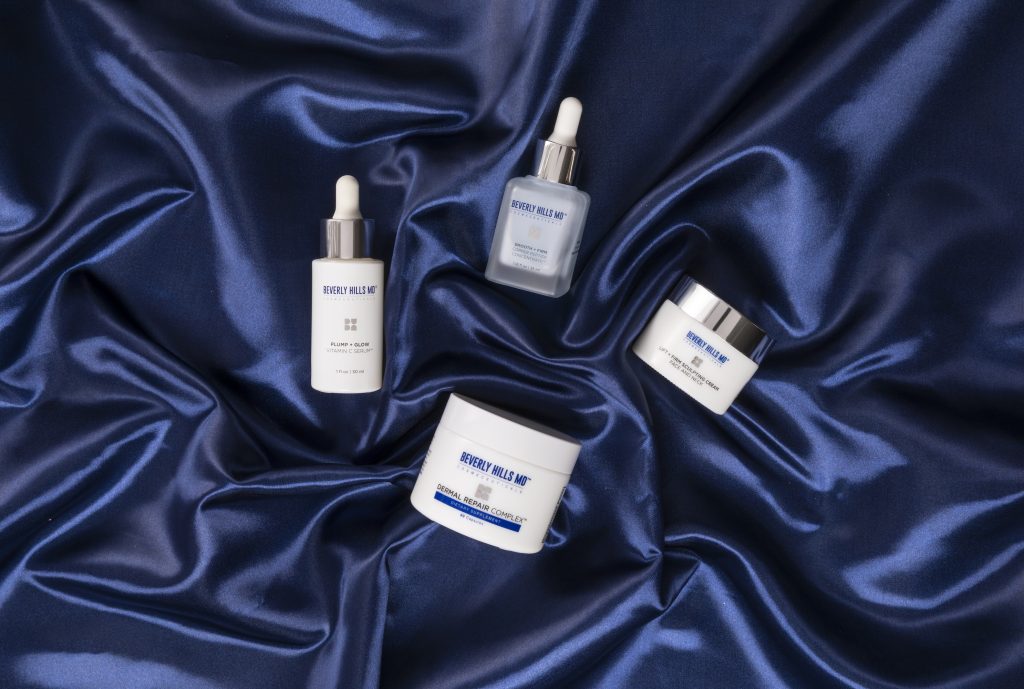Beverly Hills MD skincare products arranged on a silky navy fabric, featuring serums and a cream for skin enhancement.