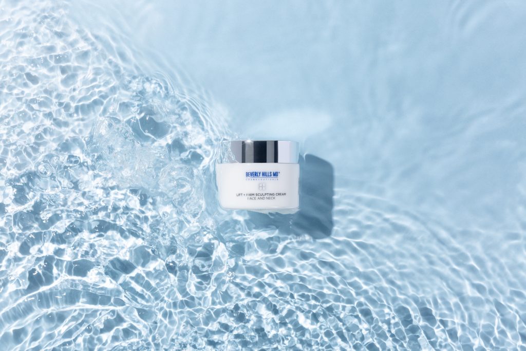 Beverly Hills MD Lift + Firm Sculpting Cream jar placed on a blue water background, highlighting its skincare benefits.