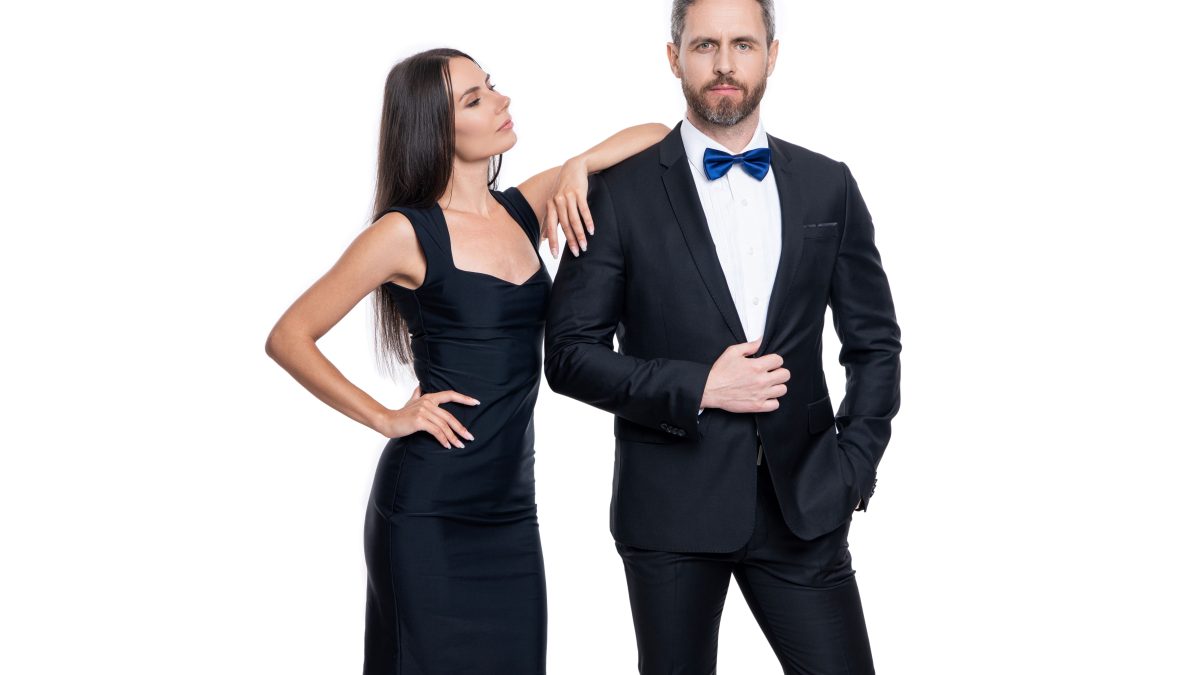 A man in a tuxedo and a woman in a black dress pose confidently, embodying elegance and modern romance.