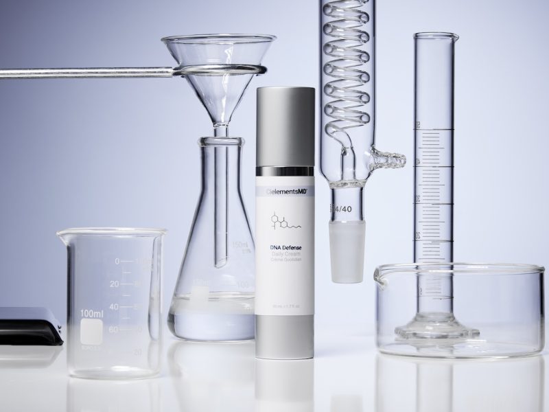 CielementsMD DNA Defense daily cream surrounded by laboratory glassware, emphasizing skincare science for UVA protection.
