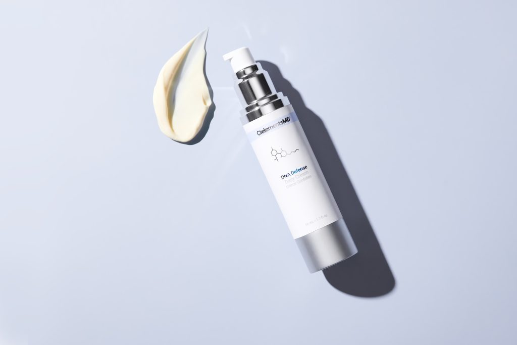 CielementsMD DNA Defender daily cream bottle next to a swirl of cream on a light background.