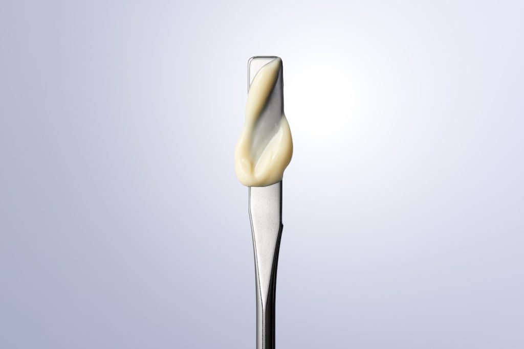 A small amount of cream is spread on a metallic spatula against a softly lit background.