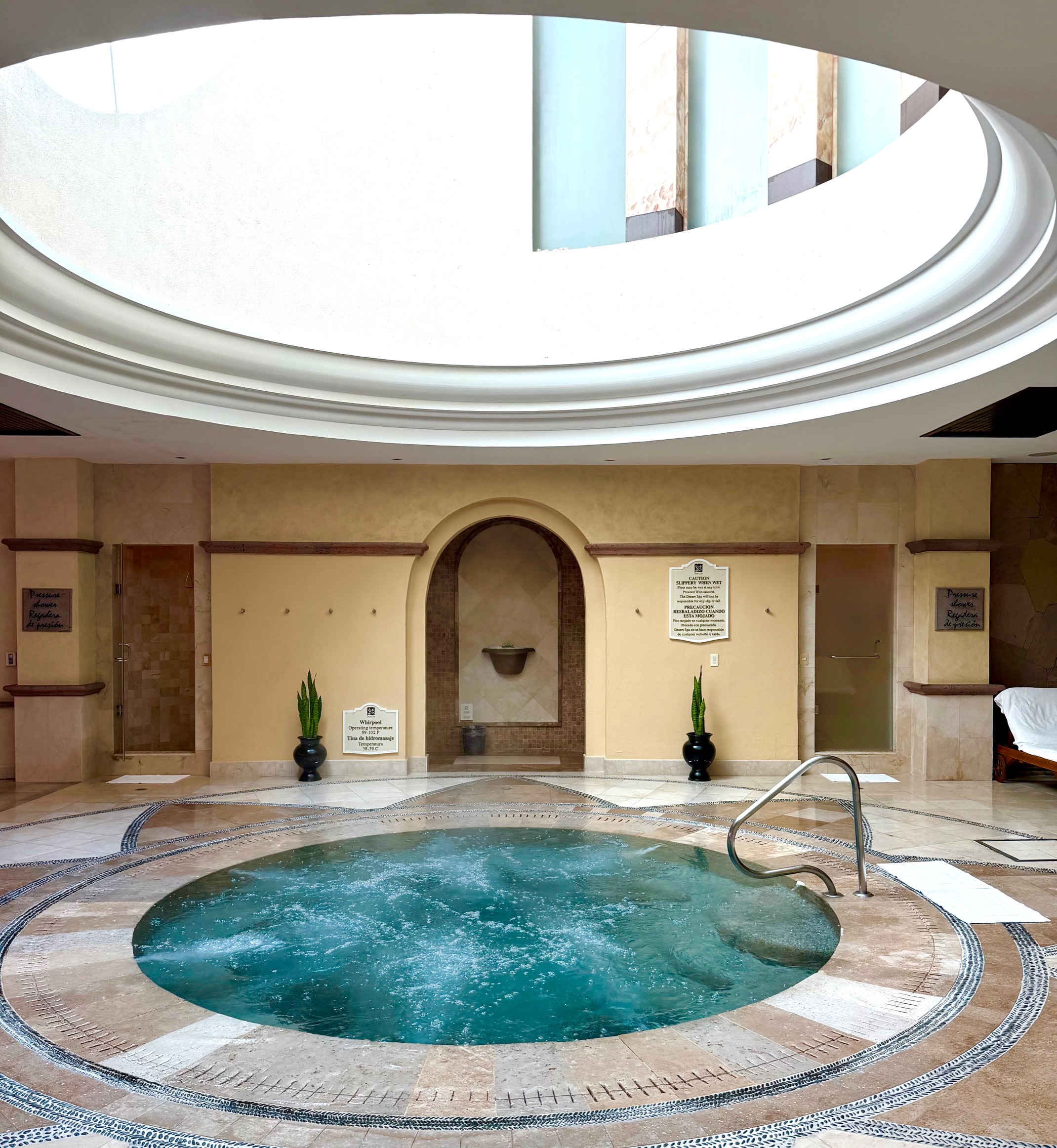Relaxation area featuring a soothing circular hot tub beneath a skylight, surrounded by elegant stone and plant accents.