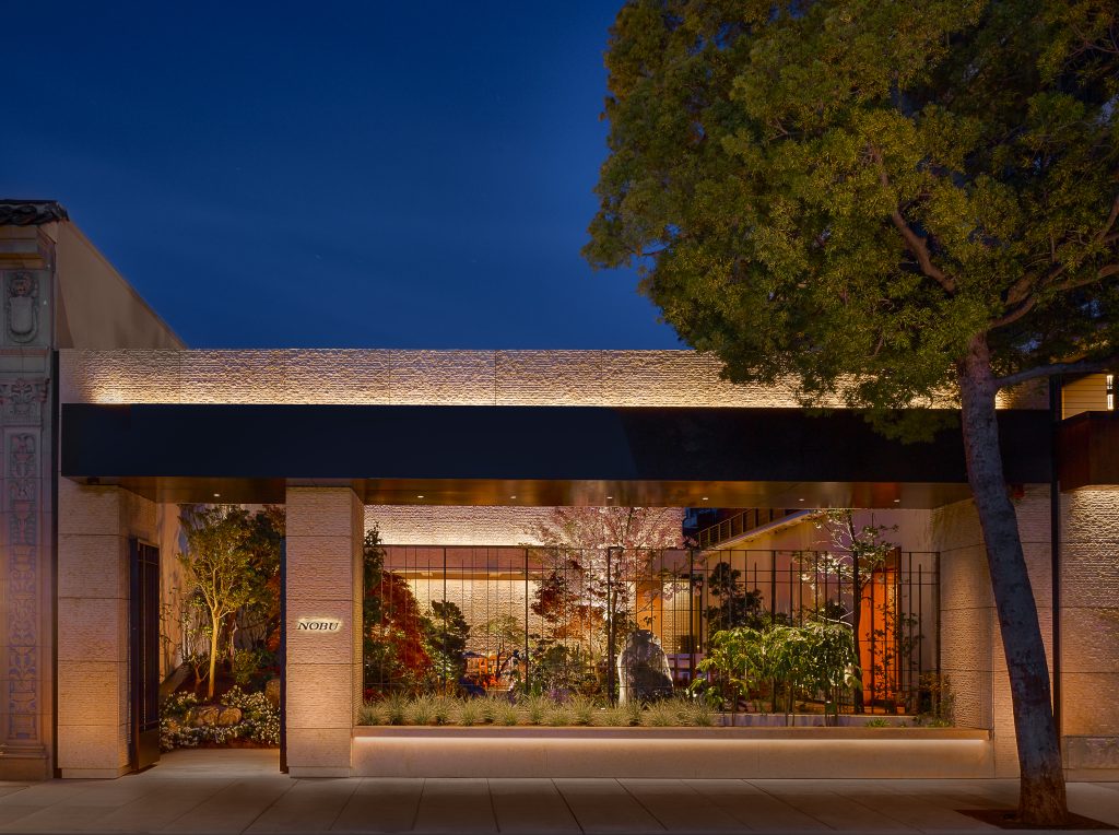 Nobu restaurant entrance at night, featuring lush greenery and a modern facade with illuminated signage.
