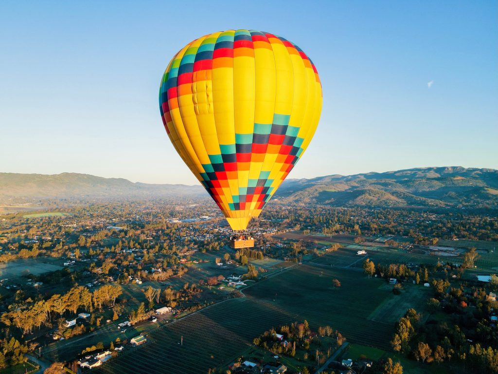 Colorful hot air balloon soaring over Sonoma County's vineyards and rolling hills at sunrise.