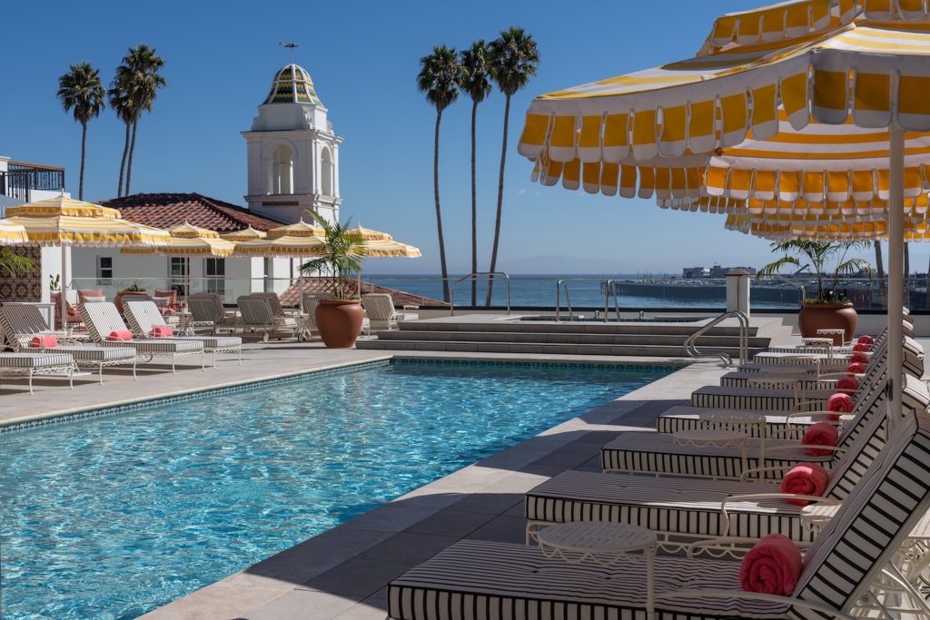 A serene plunge pool surrounded by lounge chairs and yellow umbrellas, with palm trees and ocean views in the background.