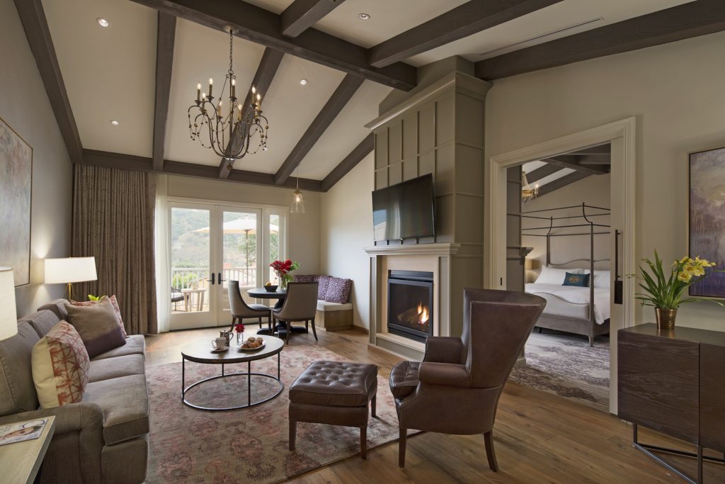 Spacious living area with fireplace, a cozy sitting space, dining table, and access to a scenic balcony in a luxurious suite.