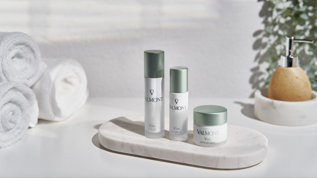 Three Valmont beauty products displayed on a marble tray, surrounded by rolled towels and a small decorative item.