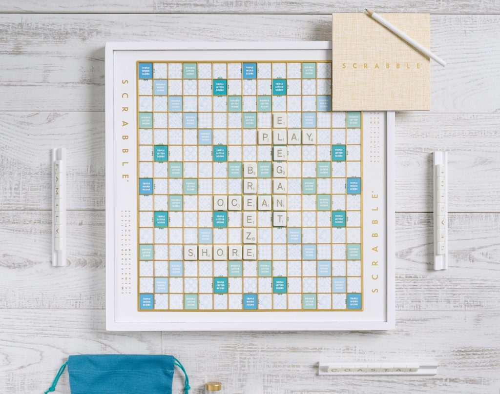Stylish Scrabble game board with coastal-themed tiles and a score pad on a light wooden surface.