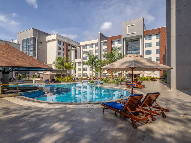 Luxurious pool area at Glee Nairobi with lounge chairs, umbrellas, and modern buildings in the background.