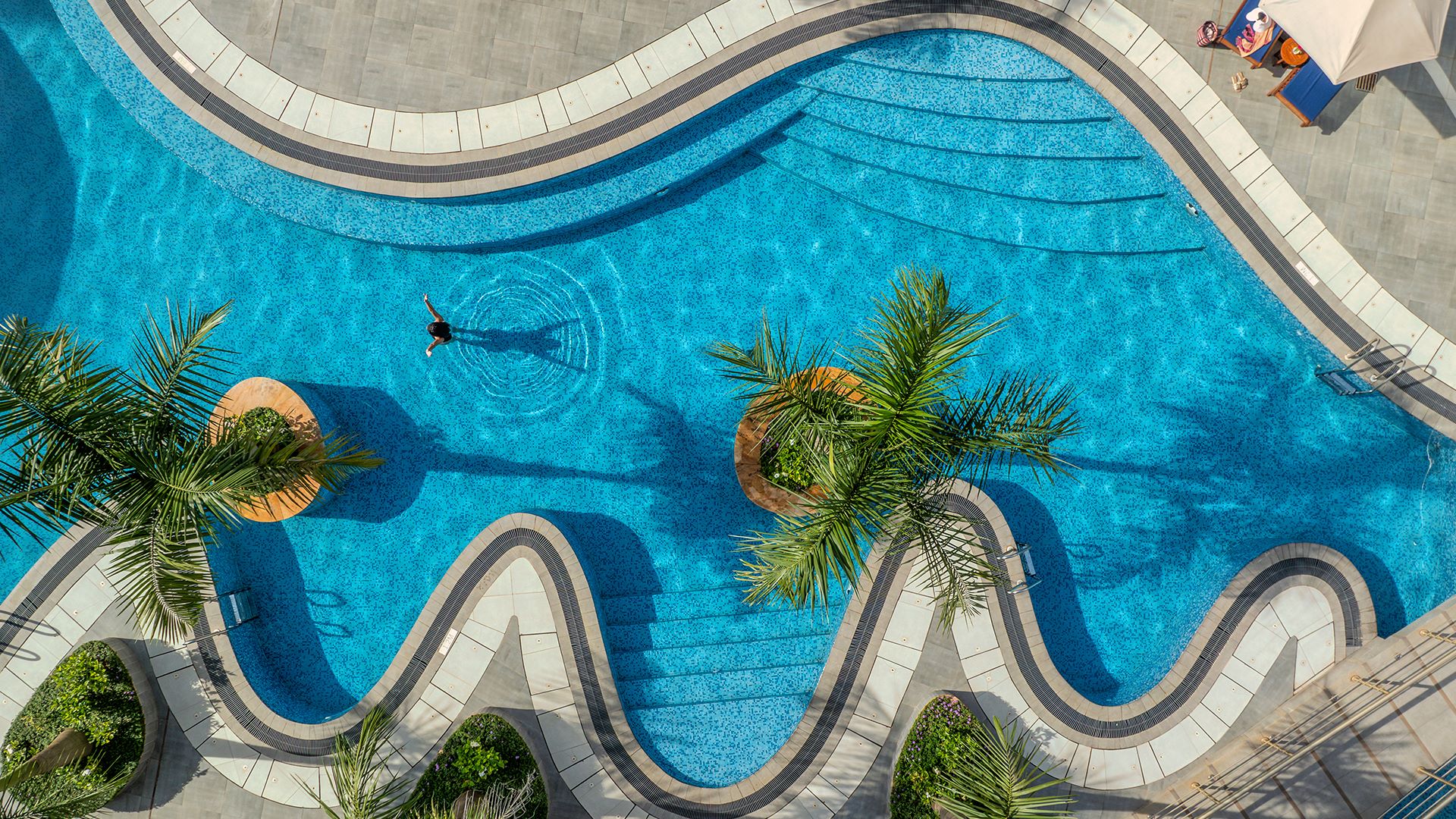 Aerial view of a winding pool surrounded by palm trees and lounge chairs at Glee Nairobi's luxury event destination.