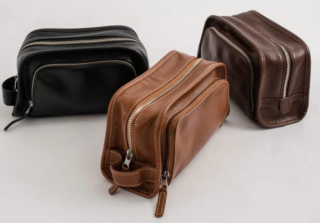 Three leather toiletry bags in black, brown, and dark brown, featuring zippered compartments and a sleek design.