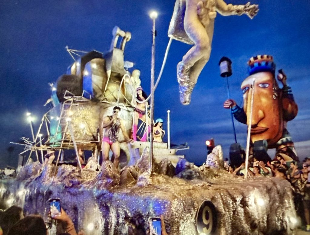 Festival float with performers and vibrant decorations during Mazatlán's Carnival, surrounded by an excited crowd.