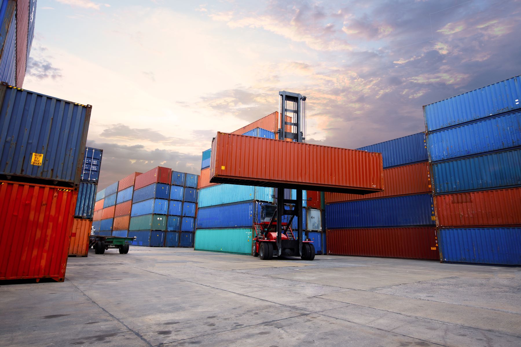A forklift lifting a large shipping container amidst brightly colored stacked containers at a storage facility.