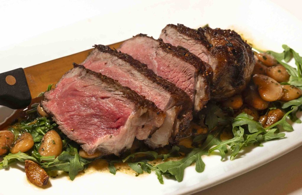 Tender slices of steak served on a bed of arugula and garnished with roasted vegetables.