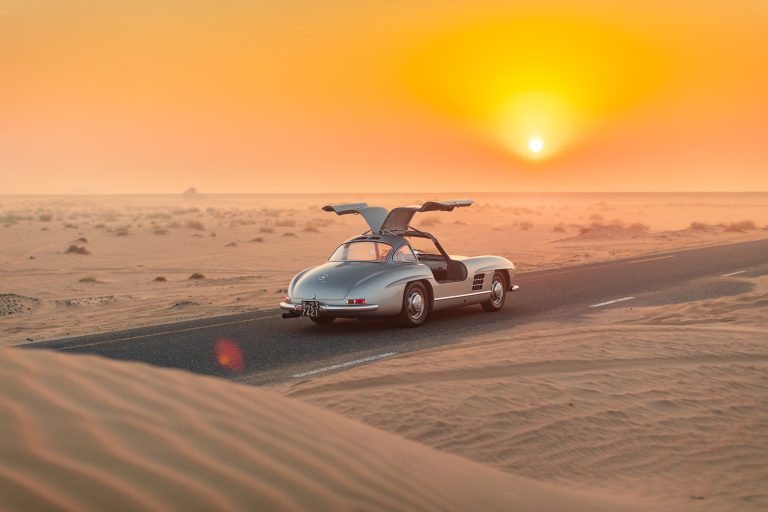 Mercedes 300 SL Gullwing parked on a desert road at sunset, showcasing its iconic design and open gullwing doors.