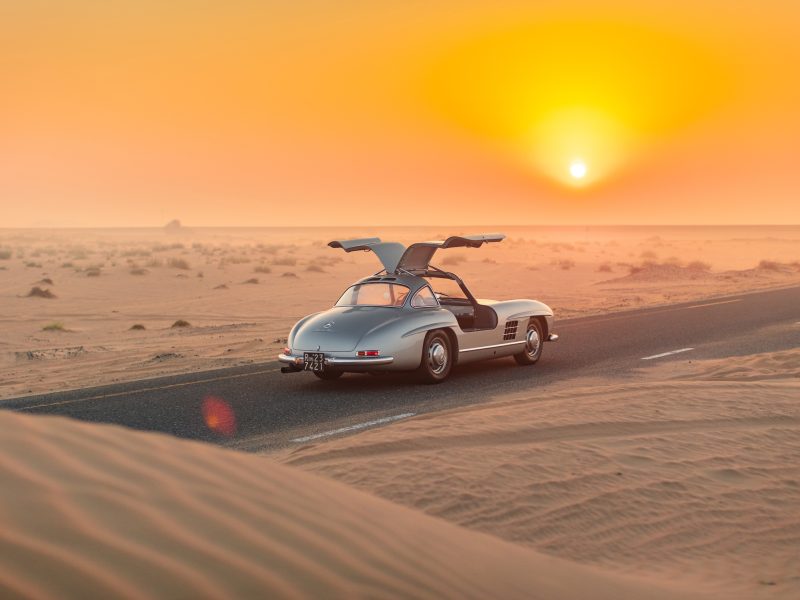 Mercedes 300 SL Gullwing parked on a desert road at sunset, showcasing its iconic design and open gullwing doors.