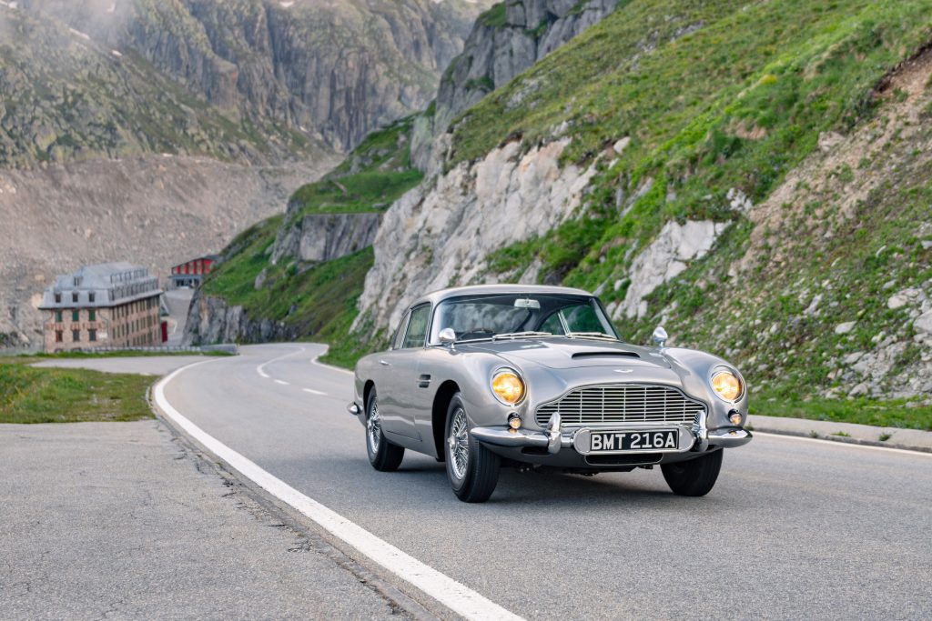 Aston Martin DB5 parked on a mountain road with rugged cliffs in the background, showcasing its classic design.