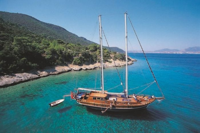 A traditional gulet sailboat anchored in turquoise waters, surrounded by lush greenery and rocky coastline in Turkiye.