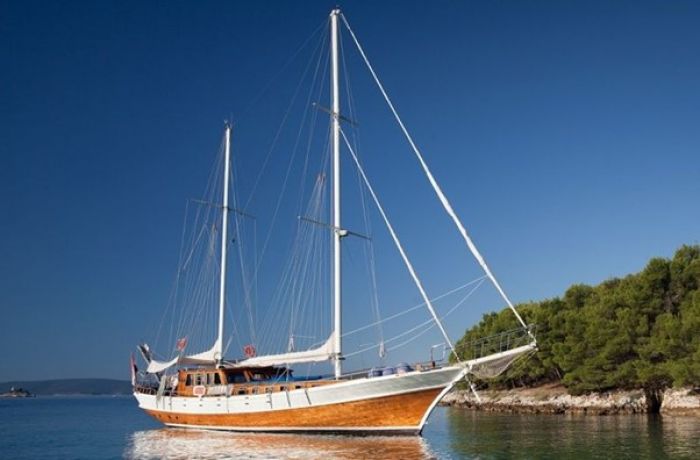 A gulet boat anchored near a lush green shoreline against a clear blue sky, illustrating cruise routes in Turkiye.