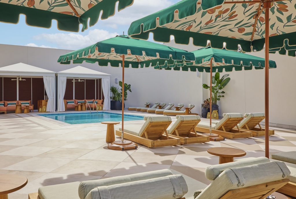 Stylish pool deck at Cameo Beverly Hills featuring cabanas, lounge chairs, and vibrant green umbrellas against a bright sky.