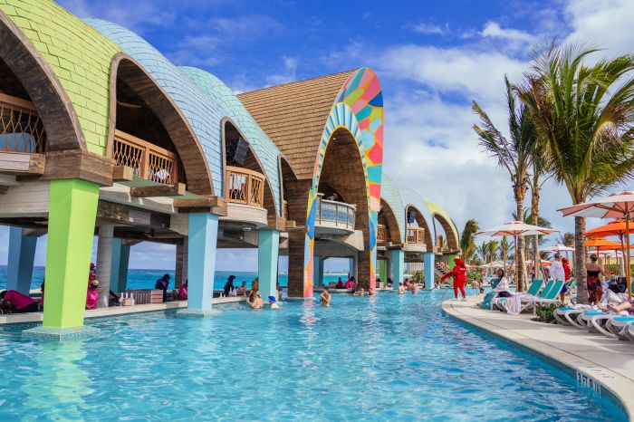 Colorful beachfront cabanas and palm trees surround a vibrant pool at Royal Caribbean's all-inclusive beach club.