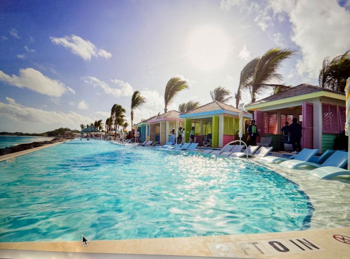 Vibrant beachfront cabanas line a sparkling pool under a sunny sky at Royal Caribbean's all-inclusive Royal Beach Club.