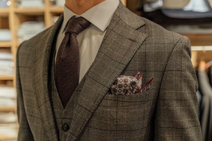 A man in a tailored gray plaid suit with a matching tie and pocket square, showcasing modern formal attire.
