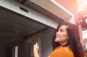 Woman using a remote control to operate a garage door, highlighting safety concerns for home garage access.