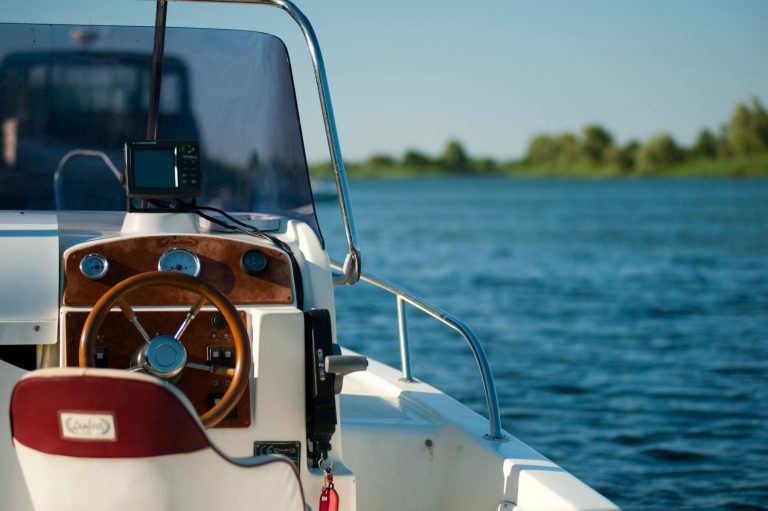 Boat dashboard featuring a wooden steering wheel and electronic displays, overlooking calm water and tree-lined banks.