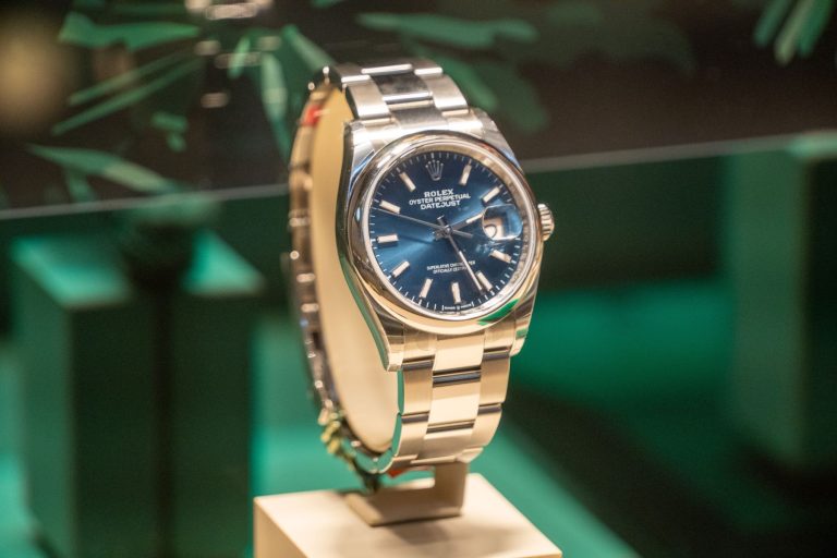 Rolex Oyster Perpetual Datejust watch displayed with a blue dial and stainless steel bracelet on a pedestal.