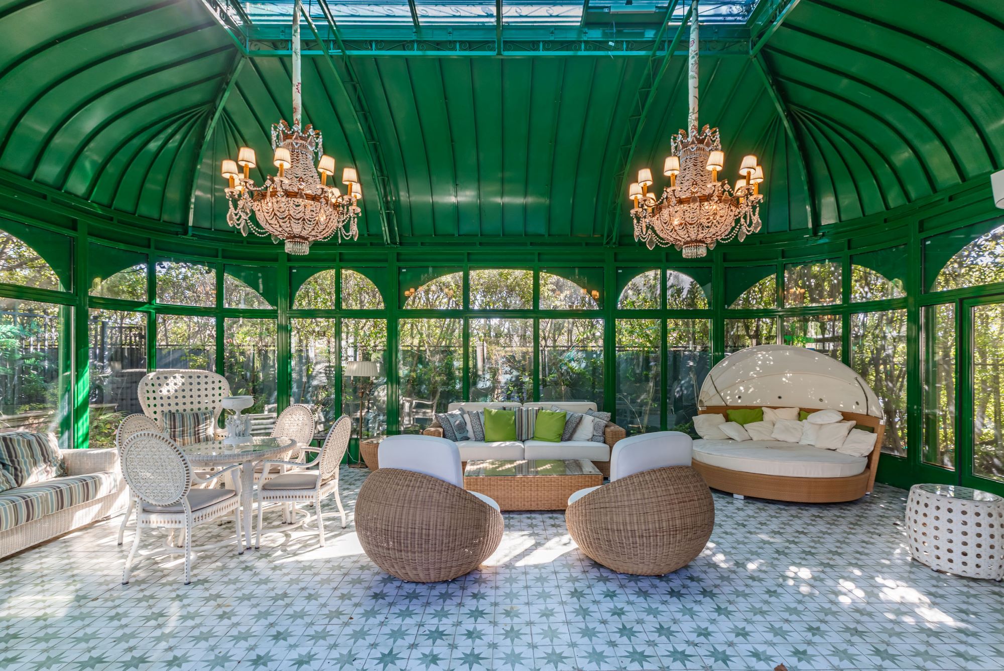 Luxurious green solarium with elegant chandeliers, stylish seating, and patterned tile flooring at the Rosewood Estate.