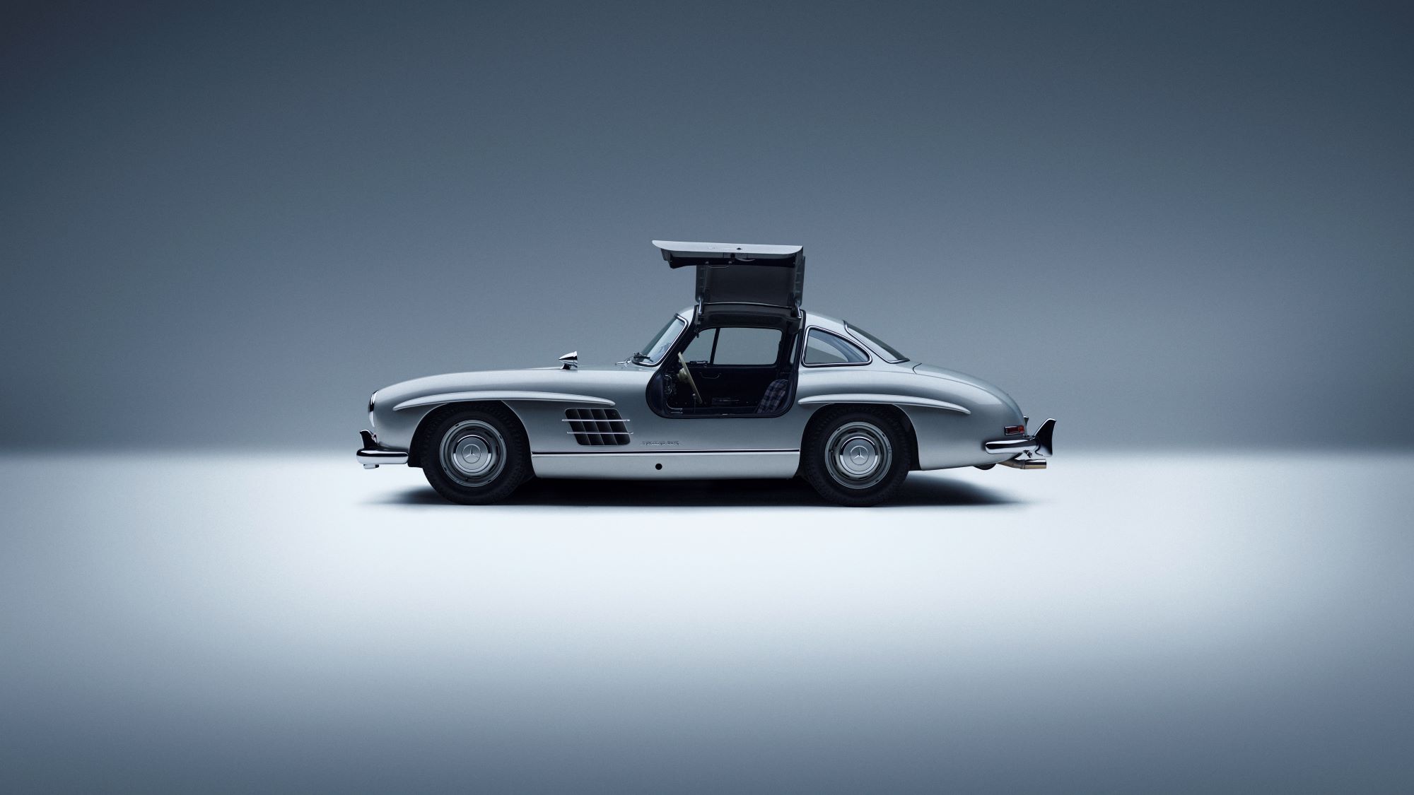 A classic Mercedes-Benz car with gullwing doors, showcasing its sleek silver design against a minimalist background.