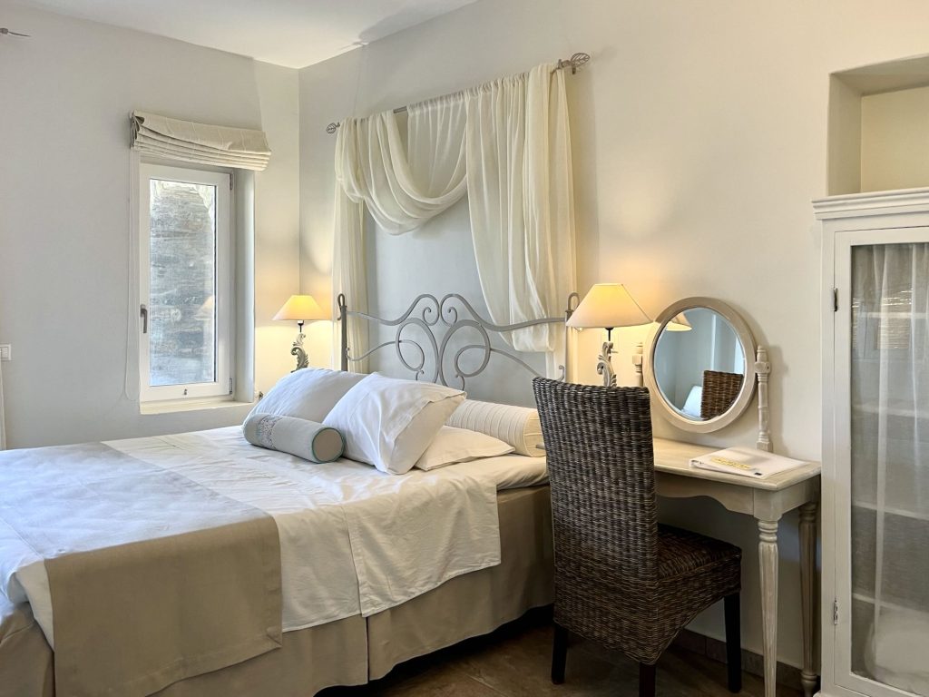 Spacious hotel room with a comfortable bed, stylish decor, and natural light, featuring a writing desk and a mirror.