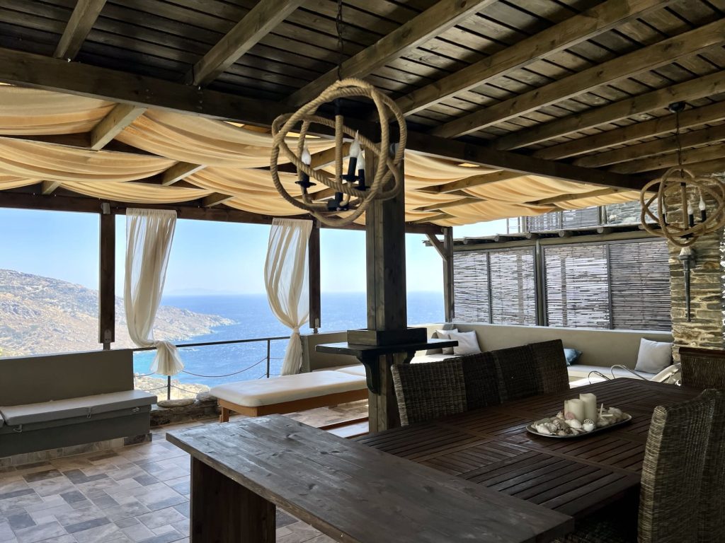 Cozy dining area with a sea view at Aegean Castle, featuring a wooden table and soft furnishings under elegant drapery.