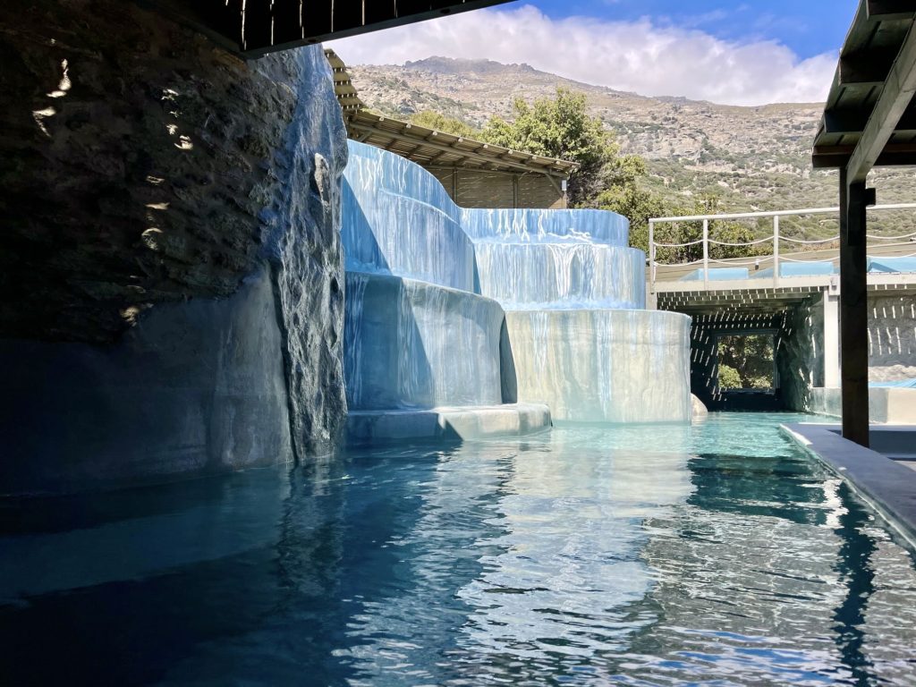 Luxury boutique hotel pool at Aegean Castle, featuring cascading water and scenic mountain views on Andros Island.