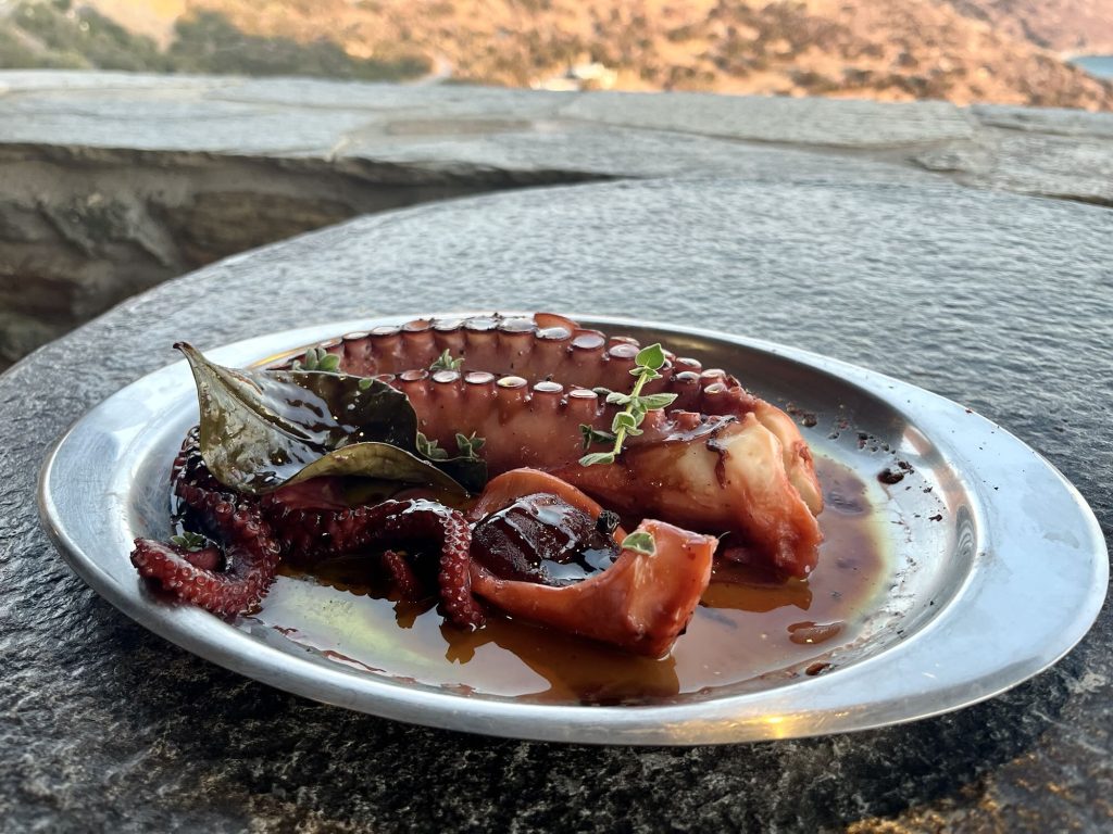 Grilled octopus served with herbs and olive oil on a silver plate, capturing the essence of Aegean cuisine.