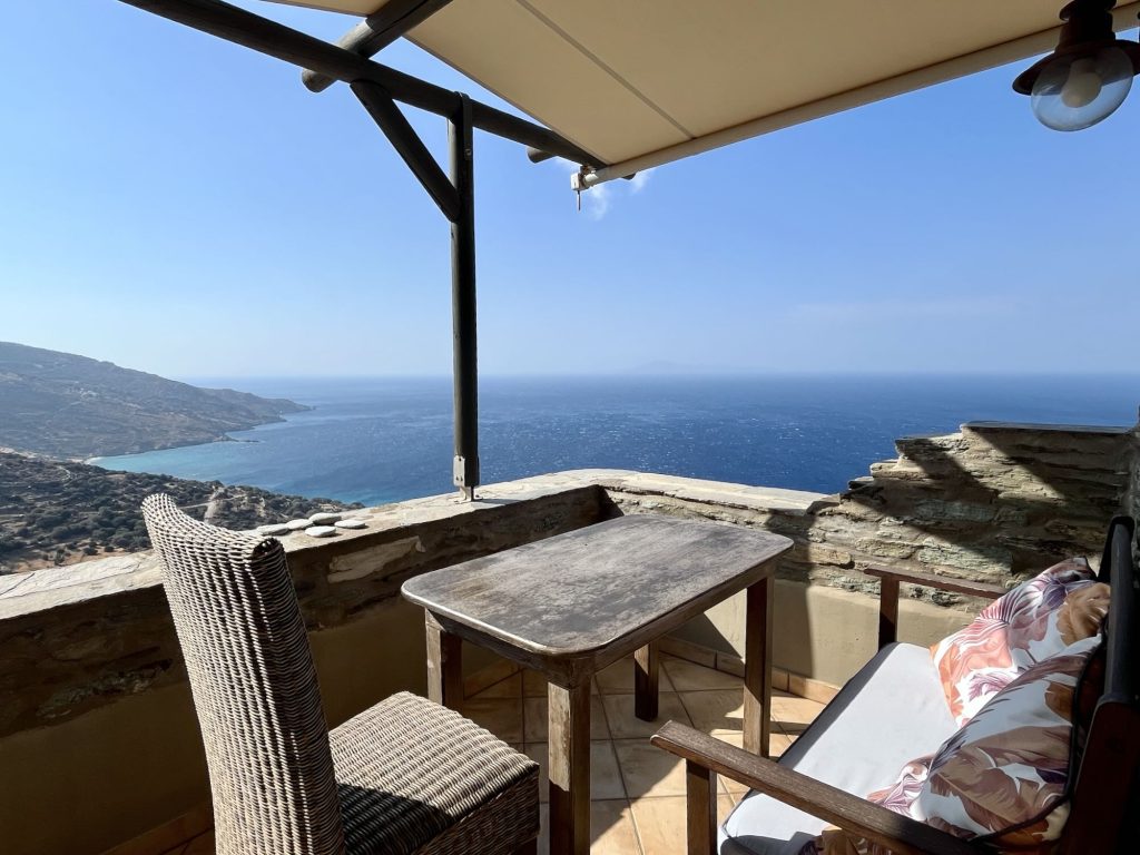 View from a terrace at Aegean Castle, featuring a table, chairs, and a stunning outlook over the sea and surrounding hills.