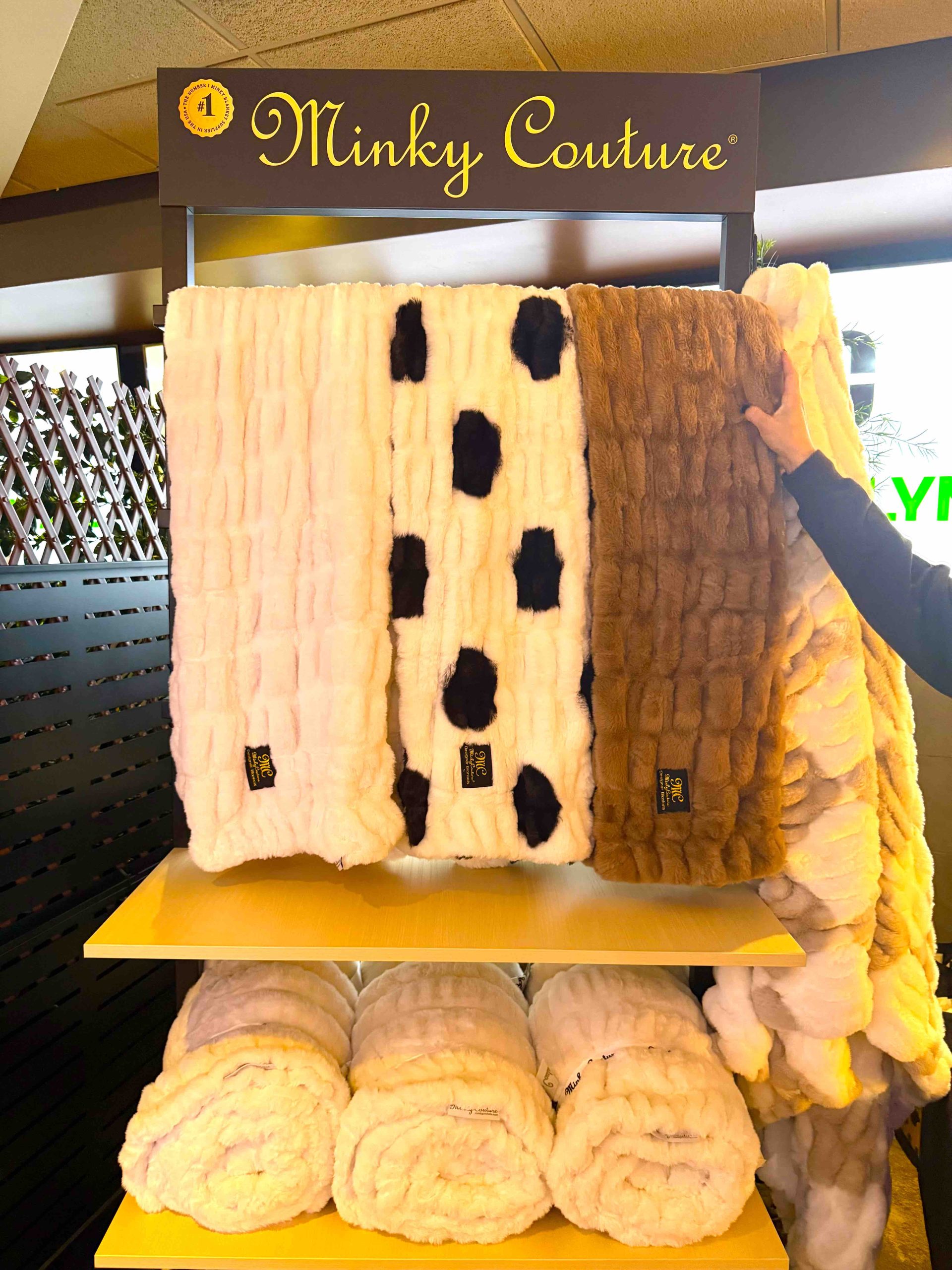 Minky Couture blankets displayed on a yellow shelf at the 2026 Grammy Awards Gift Lounge with various patterns and colors.