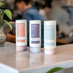 Three Wonderstate Coffee cans on a marble surface, labeled Alo Chilaka, Kangiri, and Sol Naciente, with a plant nearby.