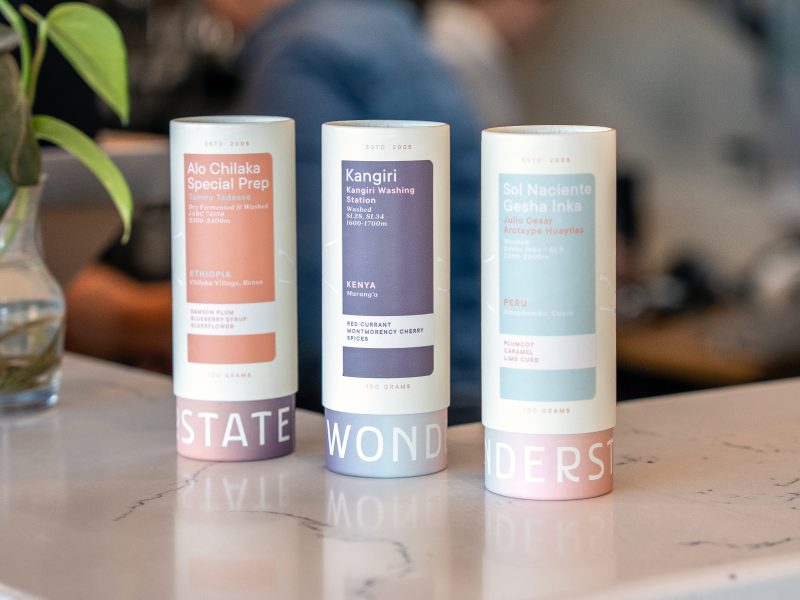 Three Wonderstate Coffee cans on a marble surface, labeled Alo Chilaka, Kangiri, and Sol Naciente, with a plant nearby.