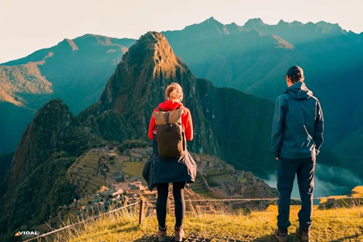 Two travelers overlook Machu Picchu with mountains and clouds in the background, highlighting the site's majestic beauty.