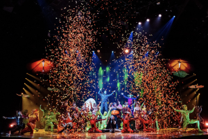 A colorful scene from Cirque du Soleil’s OVO performance with performers celebrating amid cascading confetti.