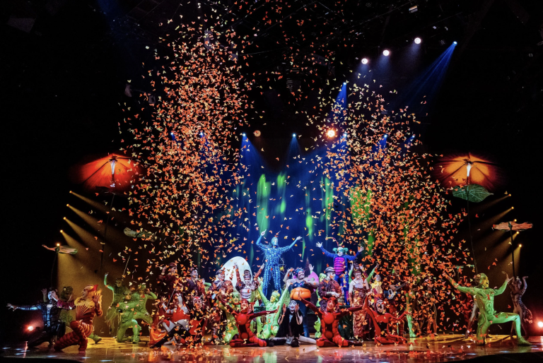 A colorful scene from Cirque du Soleil’s OVO performance with performers celebrating amid cascading confetti.
