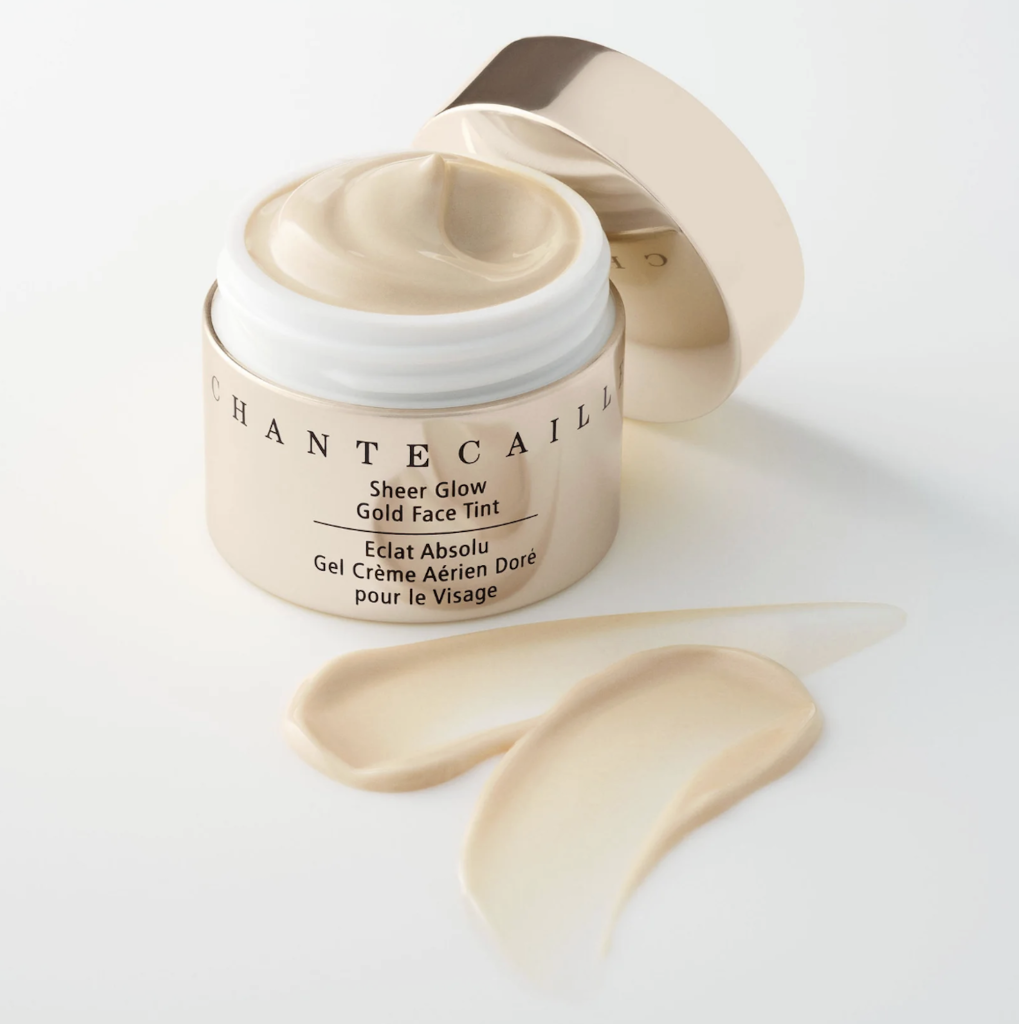 Gold face tint moisturizer in a jar with product name visible, accompanied by two swatches of the cream on a white background.