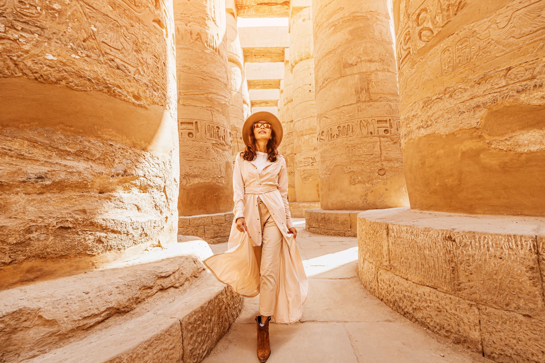 A woman walks through ancient columns in a sunlit temple, showcasing Egypt’s rich history and breathtaking architecture.