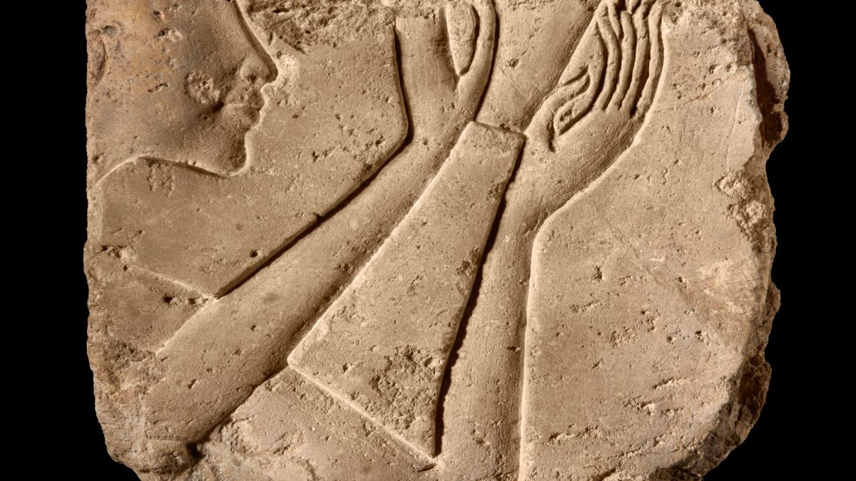 Limestone relief fragment depicting a face and hands in ancient Egyptian style, showcasing craftsmanship from antiquity.