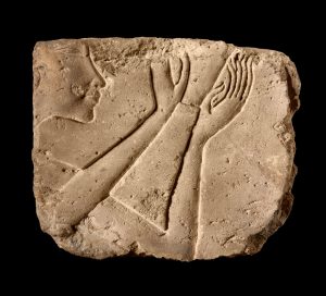 Limestone relief fragment depicting a face and hands in ancient Egyptian style, showcasing craftsmanship from antiquity.